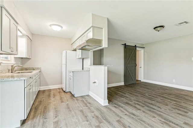 kitchen with sink, white cabinetry, light wood-type flooring, a barn door, and light stone countertops