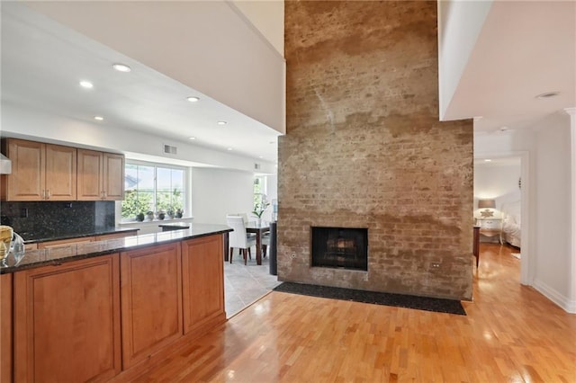 kitchen with decorative backsplash, dark stone countertops, light wood-type flooring, and a fireplace