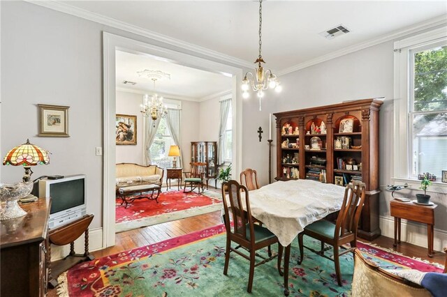 dining area featuring wood-type flooring, ornamental molding, and an inviting chandelier