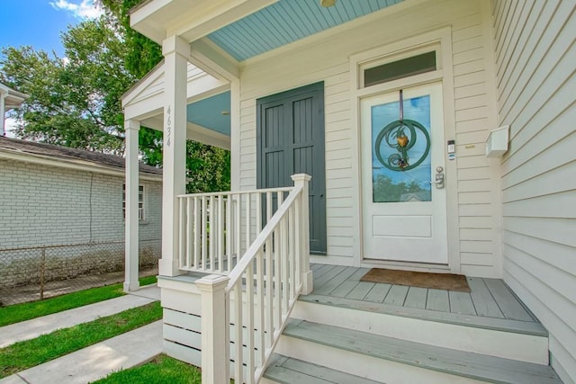 view of exterior entry featuring fence and covered porch