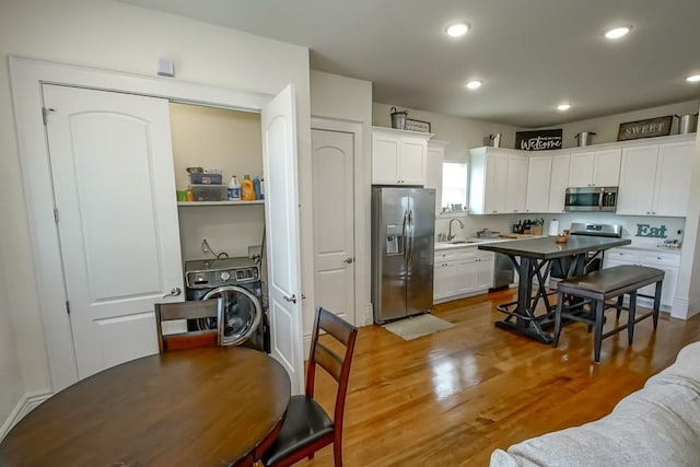 kitchen with white cabinets, sink, hardwood / wood-style flooring, washer / dryer, and stainless steel appliances