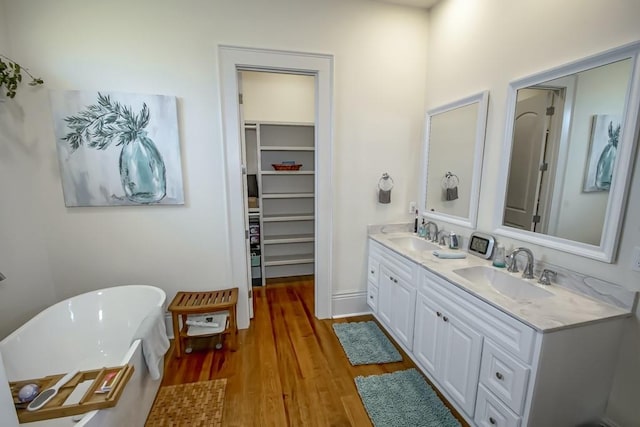 full bath featuring double vanity, a freestanding bath, wood finished floors, and a sink