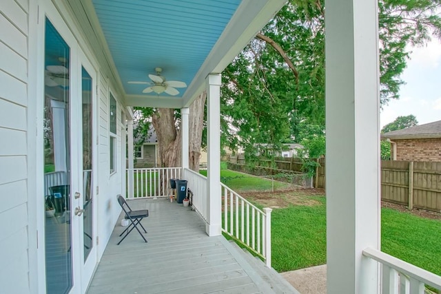 wooden terrace featuring covered porch, ceiling fan, and a lawn