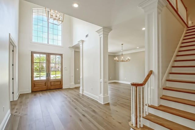 entrance foyer featuring french doors, a towering ceiling, crown molding, light hardwood / wood-style flooring, and a notable chandelier