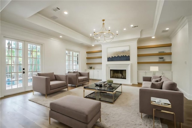 living room featuring hardwood / wood-style floors, a chandelier, a raised ceiling, and french doors