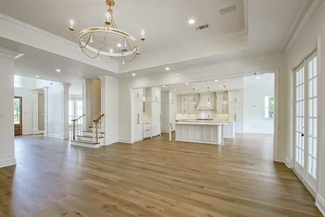 unfurnished living room featuring a chandelier, wood-type flooring, a wealth of natural light, and crown molding