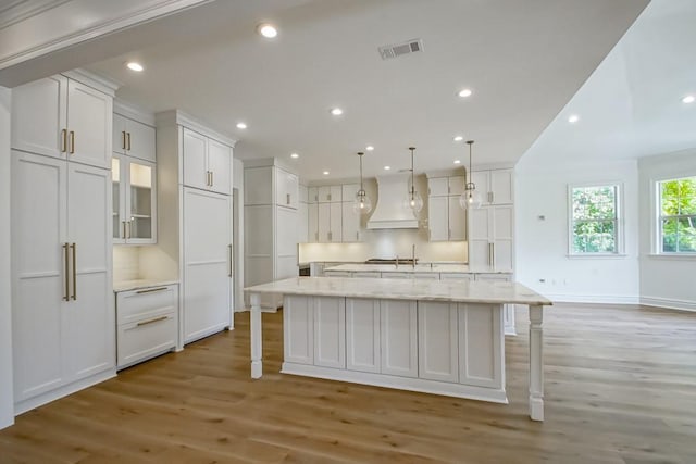 kitchen with a large island with sink, white cabinetry, light hardwood / wood-style flooring, and custom exhaust hood