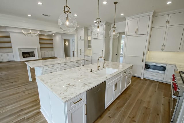 kitchen featuring sink, hanging light fixtures, stainless steel appliances, a large island with sink, and white cabinets