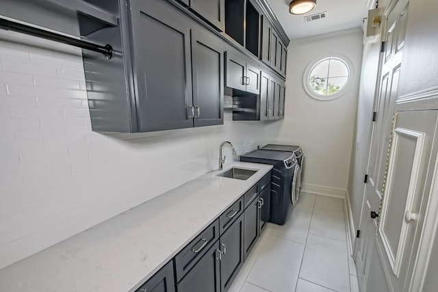 kitchen with washing machine and clothes dryer, sink, light stone counters, crown molding, and light tile patterned floors