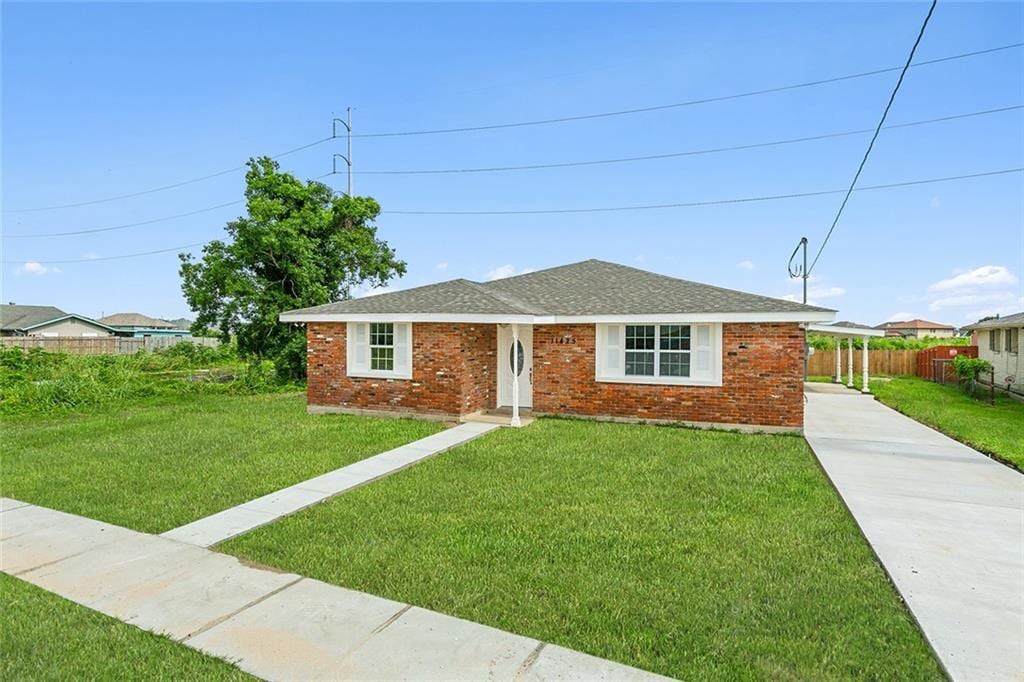 view of front of house with a shingled roof, a front yard, brick siding, and fence