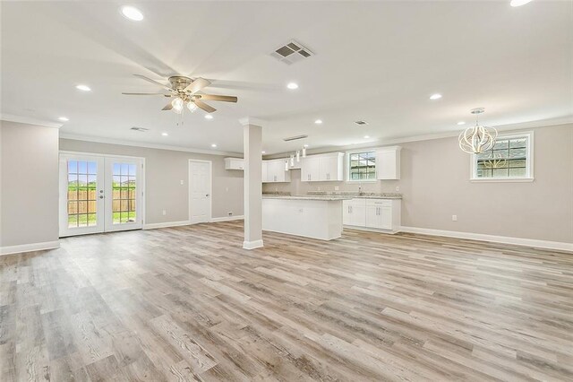 unfurnished living room featuring ceiling fan with notable chandelier, light hardwood / wood-style floors, crown molding, and french doors