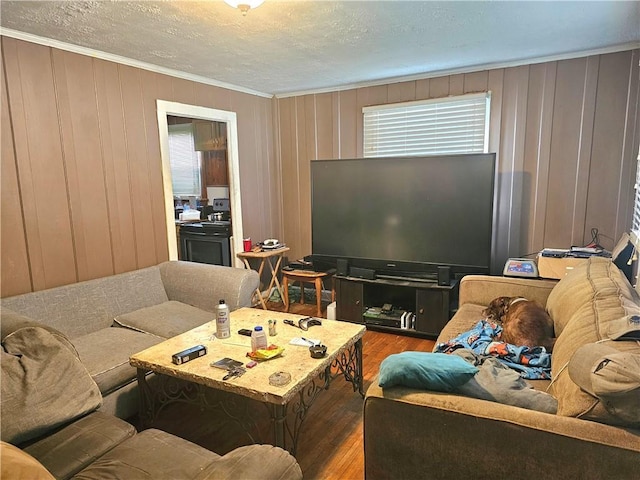 living room featuring a healthy amount of sunlight, wood walls, wood-type flooring, a textured ceiling, and ornamental molding