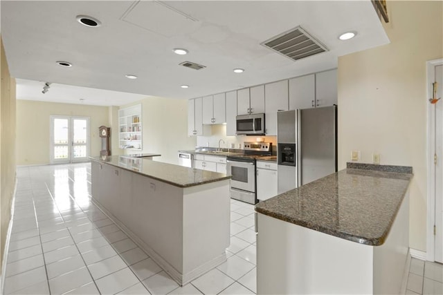 kitchen featuring appliances with stainless steel finishes, sink, white cabinets, light tile patterned floors, and kitchen peninsula