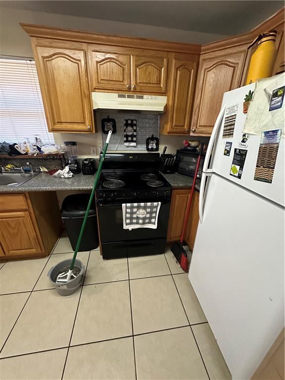 kitchen with sink, white fridge, black range oven, and light tile floors