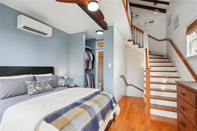 bedroom with a wall unit AC, ceiling fan, light hardwood / wood-style flooring, beamed ceiling, and a closet