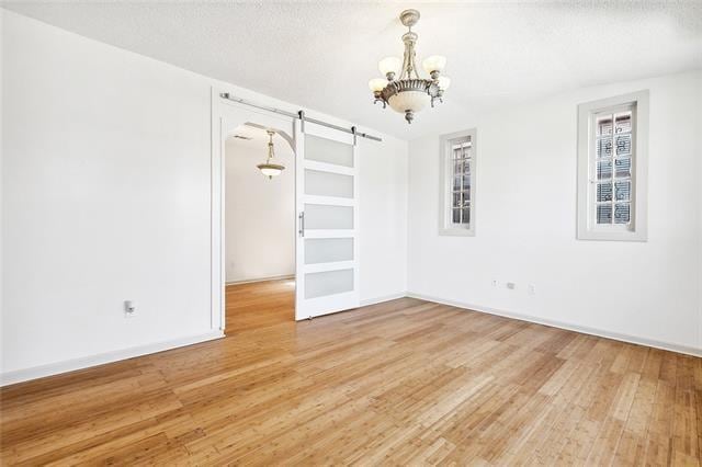 spare room with an inviting chandelier, hardwood / wood-style floors, a barn door, and a textured ceiling