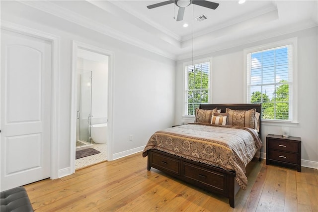 bedroom with visible vents, multiple windows, light wood-style flooring, and a tray ceiling