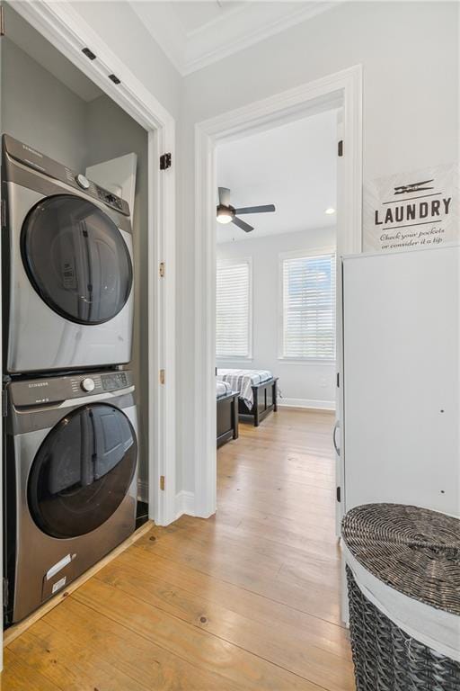 laundry area featuring stacked washer and clothes dryer, light wood-style flooring, ornamental molding, baseboards, and laundry area