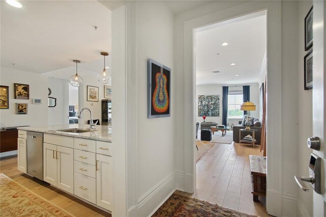 kitchen with sink, decorative light fixtures, light hardwood / wood-style flooring, dishwasher, and light stone countertops