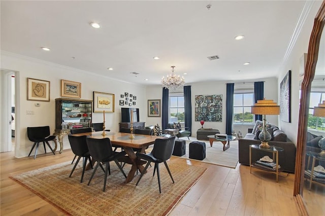 dining space with ornamental molding, light wood-type flooring, and an inviting chandelier