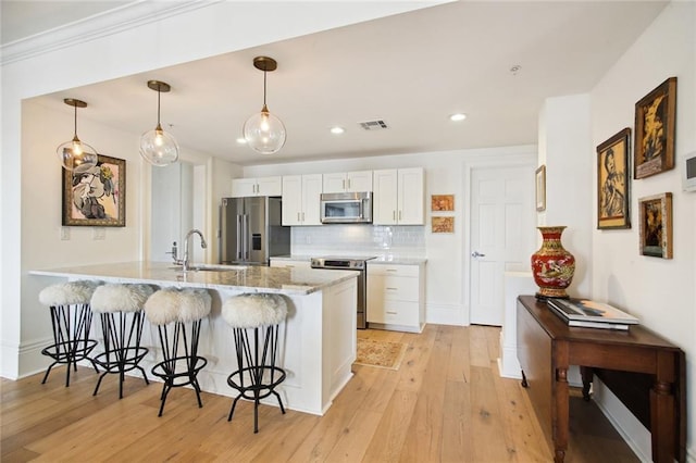 kitchen with decorative light fixtures, white cabinetry, sink, stainless steel appliances, and light stone countertops