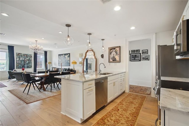 kitchen with pendant lighting, sink, appliances with stainless steel finishes, light stone counters, and white cabinets