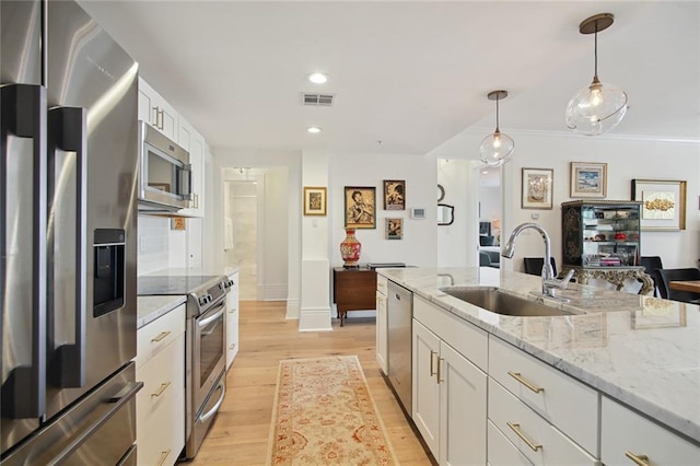 kitchen featuring appliances with stainless steel finishes, pendant lighting, sink, white cabinets, and light stone countertops