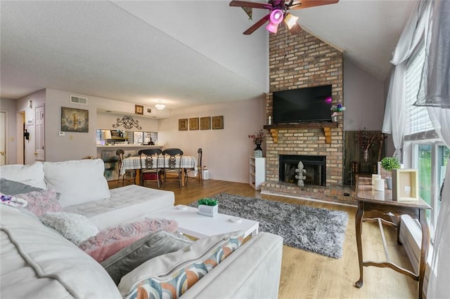 living room with ceiling fan, vaulted ceiling, a brick fireplace, brick wall, and hardwood / wood-style flooring