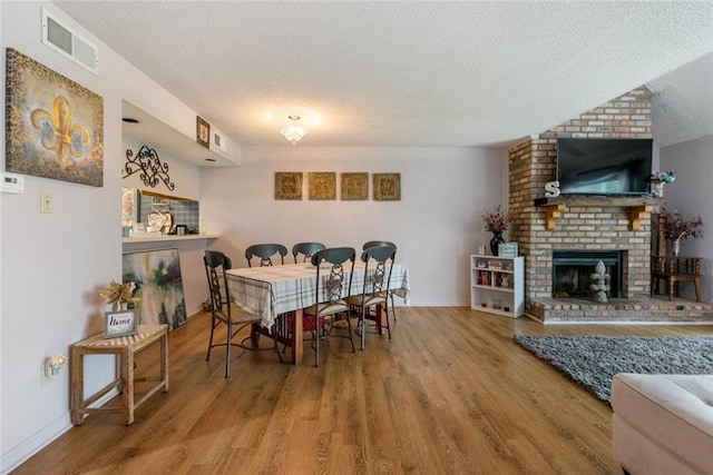 dining space featuring a textured ceiling, brick wall, wood-type flooring, and a brick fireplace