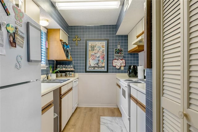 kitchen with backsplash, light wood-type flooring, sink, white appliances, and a textured ceiling