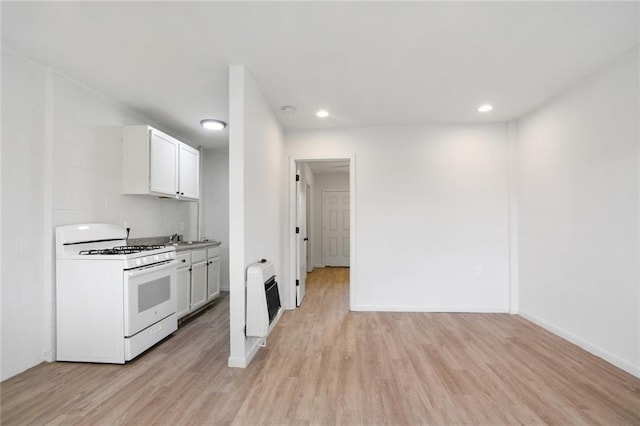 kitchen with light hardwood / wood-style flooring, heating unit, white cabinets, and gas range gas stove