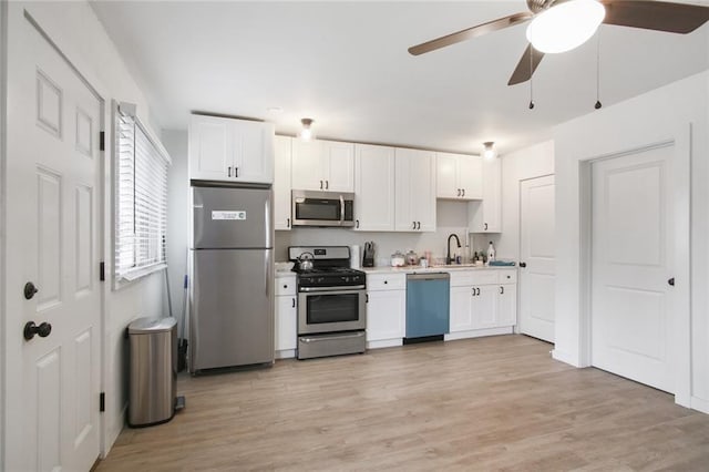 kitchen featuring appliances with stainless steel finishes, white cabinetry, ceiling fan, light hardwood / wood-style flooring, and sink