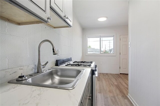 3300 Baronne St, New Orleans, LA 70115 - kitchen with white gas range oven, light stone counters, a sink, light wood-style floors, and decorative backsplash