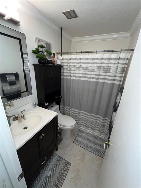 bathroom featuring vanity, a textured ceiling, a shower with shower curtain, ornamental molding, and toilet