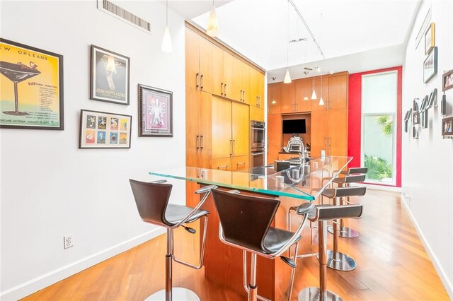 kitchen featuring hanging light fixtures, stainless steel double oven, light wood-type flooring, and kitchen peninsula