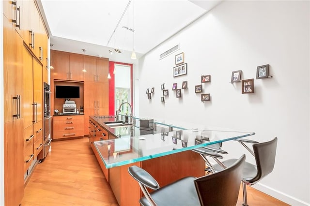 kitchen featuring light hardwood / wood-style floors, kitchen peninsula, hanging light fixtures, sink, and double oven