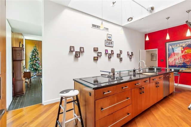 kitchen with a center island with sink, light hardwood / wood-style flooring, decorative light fixtures, sink, and dishwasher