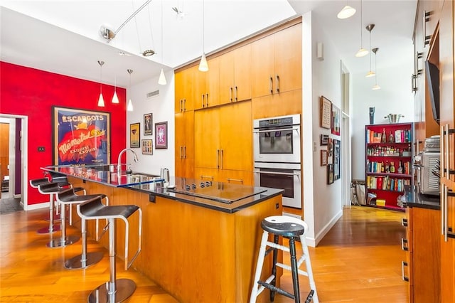 kitchen with double oven, light hardwood / wood-style flooring, a kitchen bar, sink, and pendant lighting