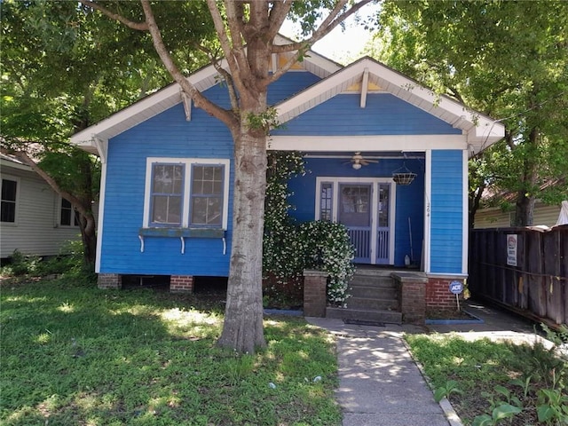 bungalow-style home with fence, covered porch, and a front yard