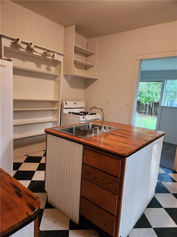 kitchen featuring open shelves, a sink, tile patterned floors, wood counters, and white range with gas stovetop