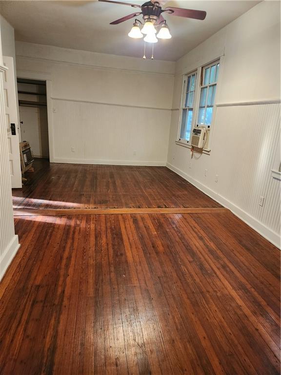 empty room with a ceiling fan, a wainscoted wall, baseboards, wood-type flooring, and cooling unit
