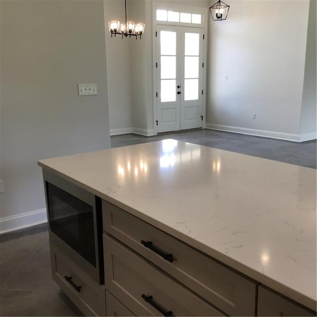 kitchen with stainless steel microwave, pendant lighting, light stone countertops, and dark tile patterned flooring