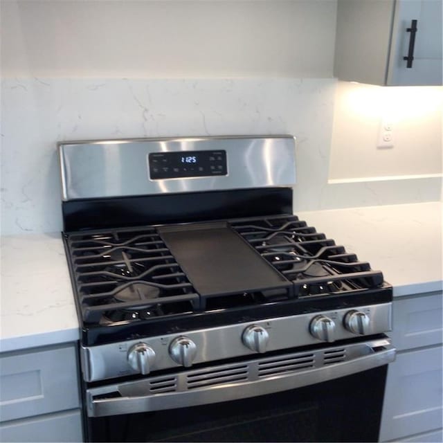 room details featuring decorative backsplash, stainless steel range with gas stovetop, and light stone countertops