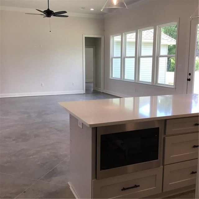 kitchen featuring ceiling fan, tile patterned floors, white cabinetry, stainless steel microwave, and crown molding