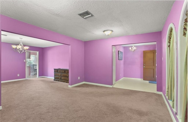 carpeted empty room with a notable chandelier and a textured ceiling