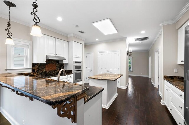 kitchen featuring tasteful backsplash, dark wood-type flooring, a center island, ornamental molding, and stainless steel double oven