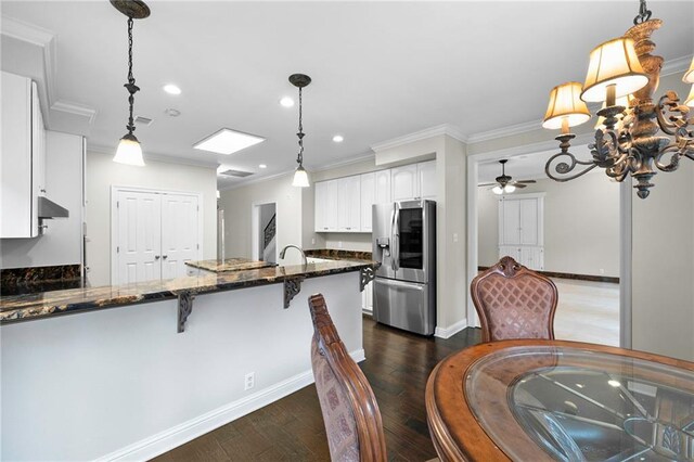 kitchen with decorative light fixtures, dark hardwood / wood-style flooring, stainless steel fridge, dark stone countertops, and white cabinets