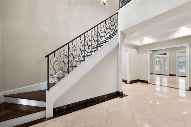 staircase with a high ceiling, a raised ceiling, and light tile floors