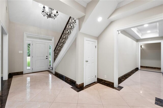 entryway with a tray ceiling, a notable chandelier, and light tile floors