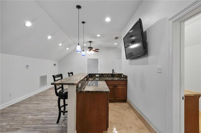 kitchen featuring a kitchen breakfast bar, ceiling fan, light wood-type flooring, dark stone countertops, and a kitchen island